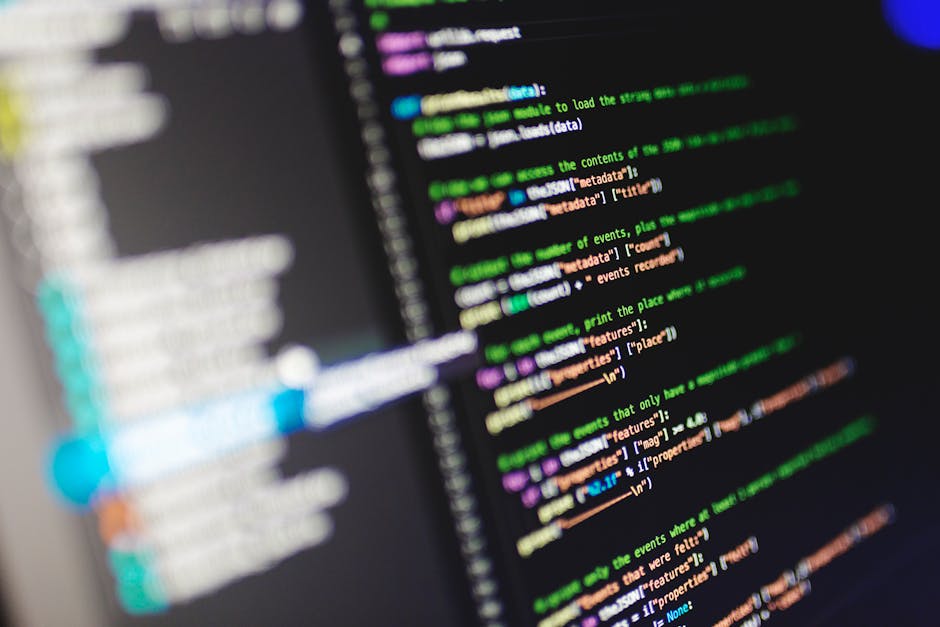 Close-up image of a laptop keyboard and screen displaying a code editor with colorful syntax highlighting, situated in a well-lit workspace. The keyboard features black keys with white lettering, and 